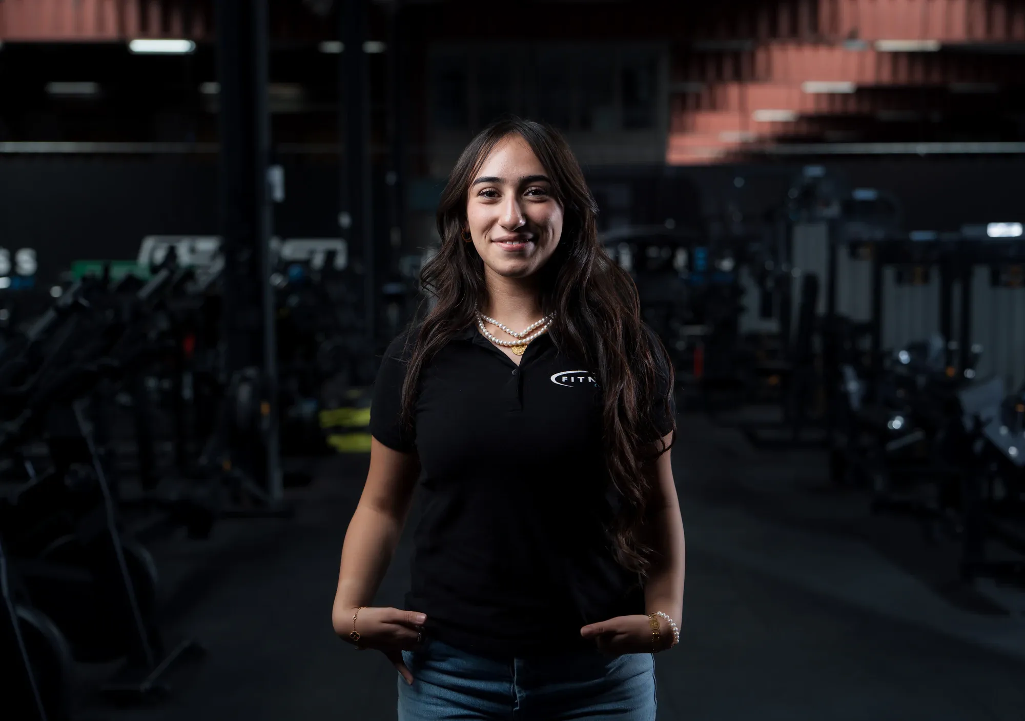 Medewerker in een zwarte polo van Fitness Company staat glimlachend in de donkere showroom