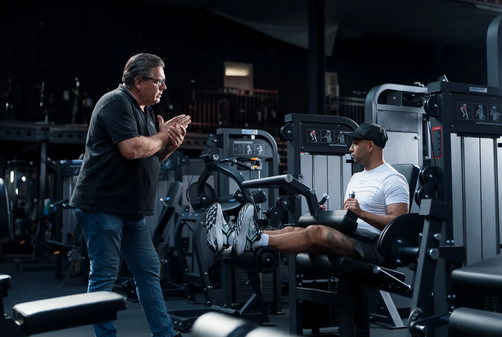 Medewerker van Fitness Company geeft uitleg aan een sporter die een beenstrektoestel uitprobeert