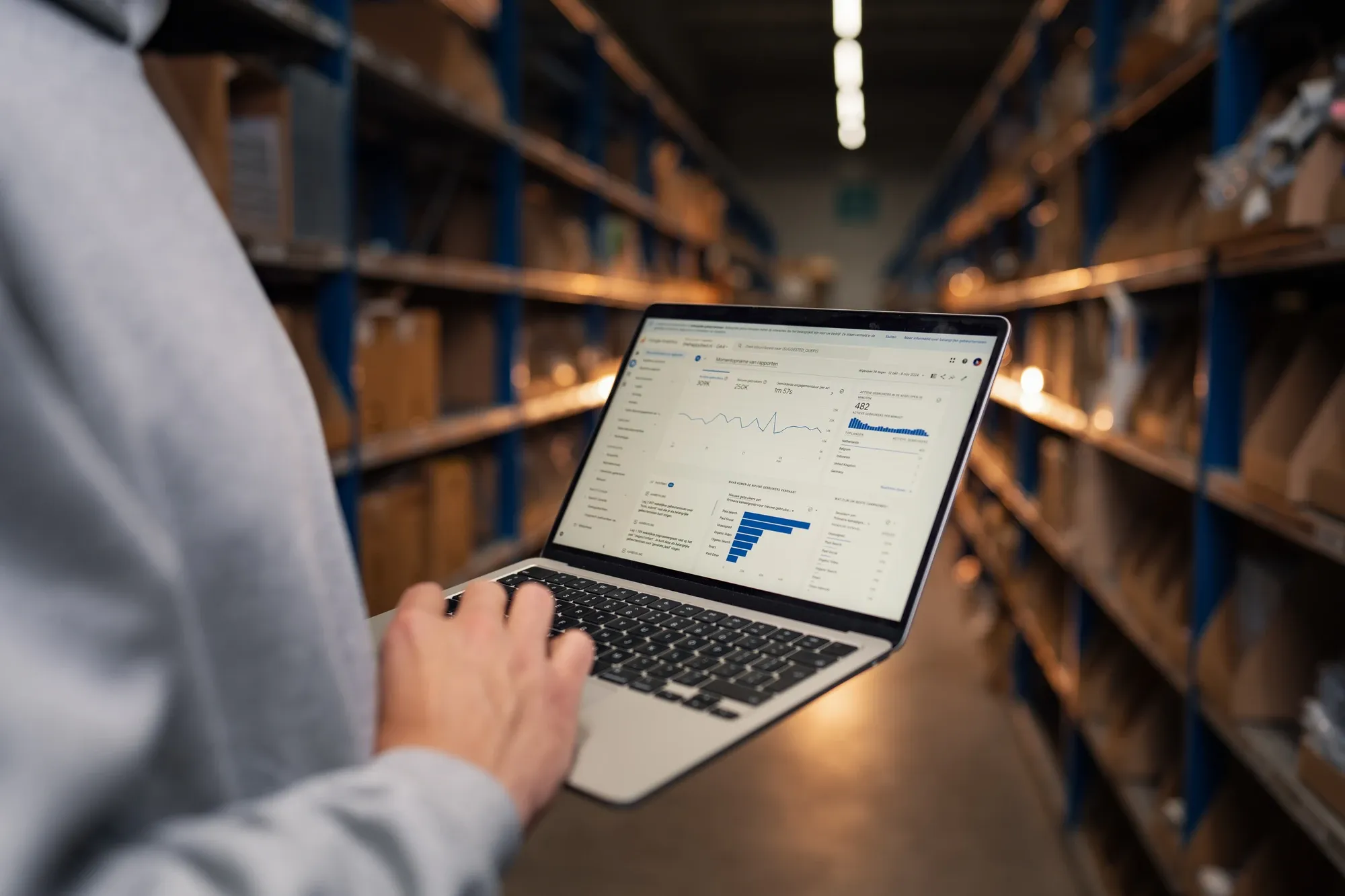 Laptop met een dashboard vol grafieken in de hand van een specialist, in een gangpad van een magazijn