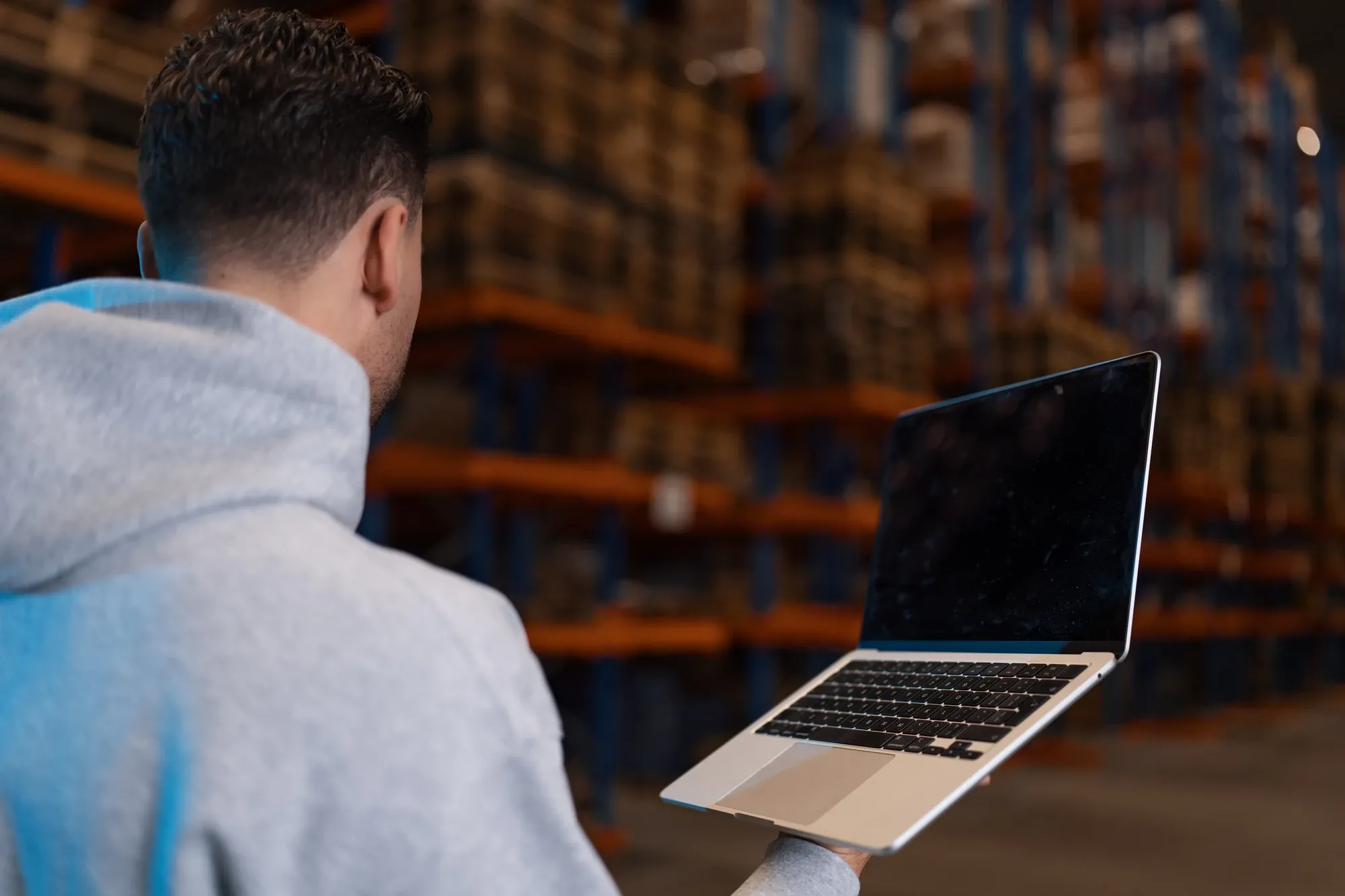 Opengeklapte laptop in de hand van een specialist van Klubb, over zijn schouder gezien, in een magazijn