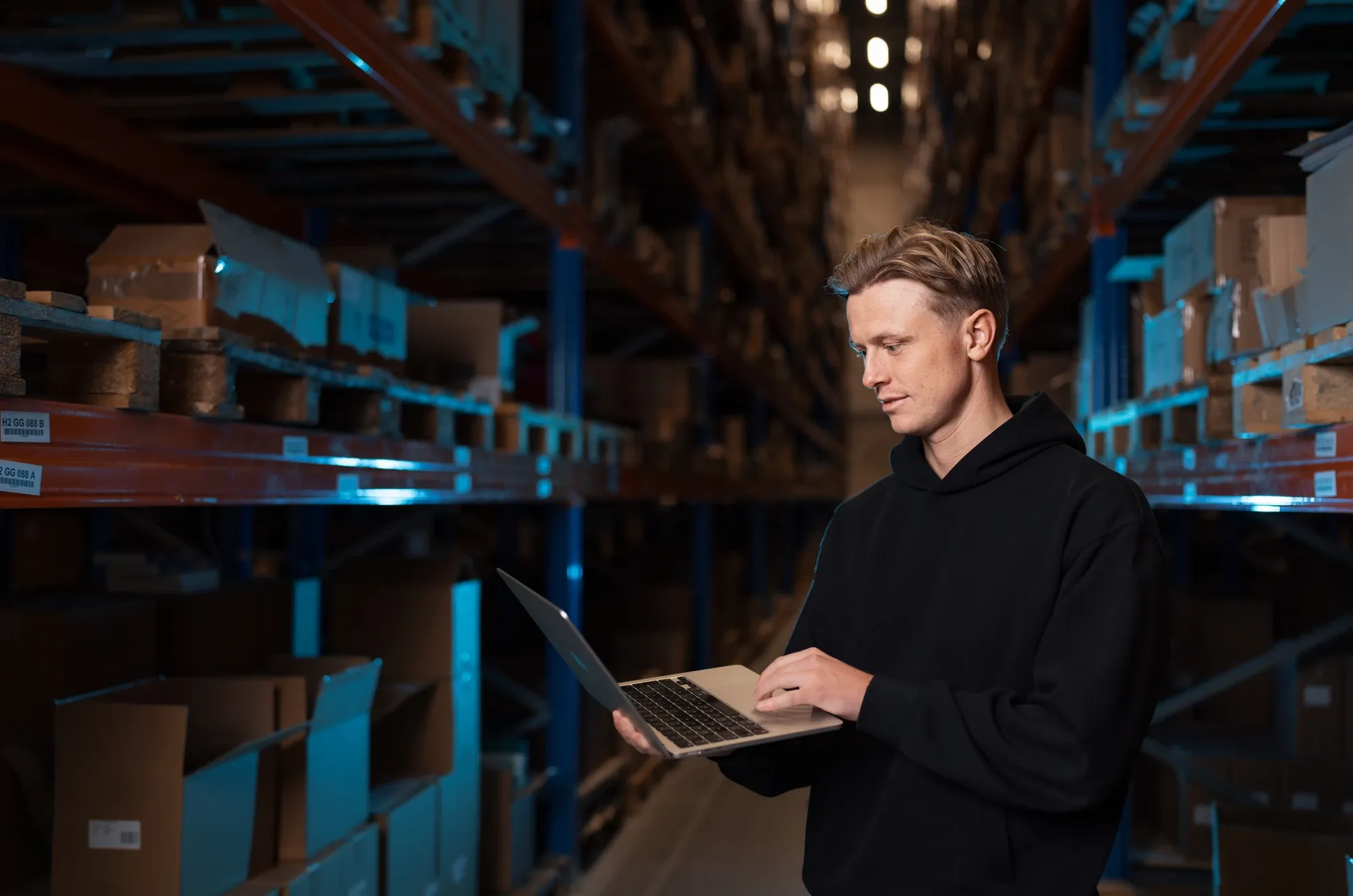 Specialist van Klubb kijkt op zijn laptop tussen de stellingen van een magazijn