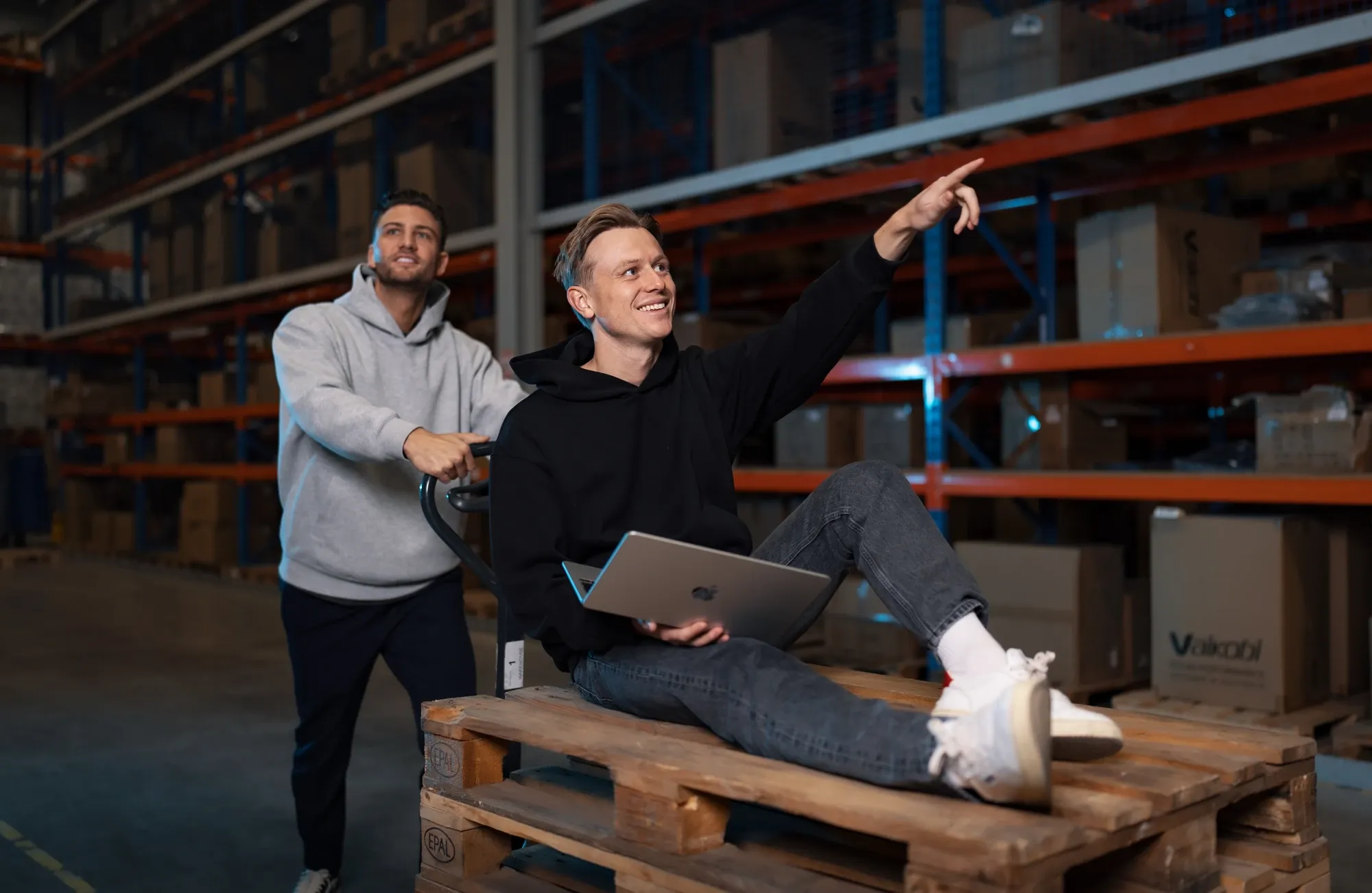 Twee specialisten van Klubb op een stapel pallets in een magazijn, een van hen wijst naar de stellingen