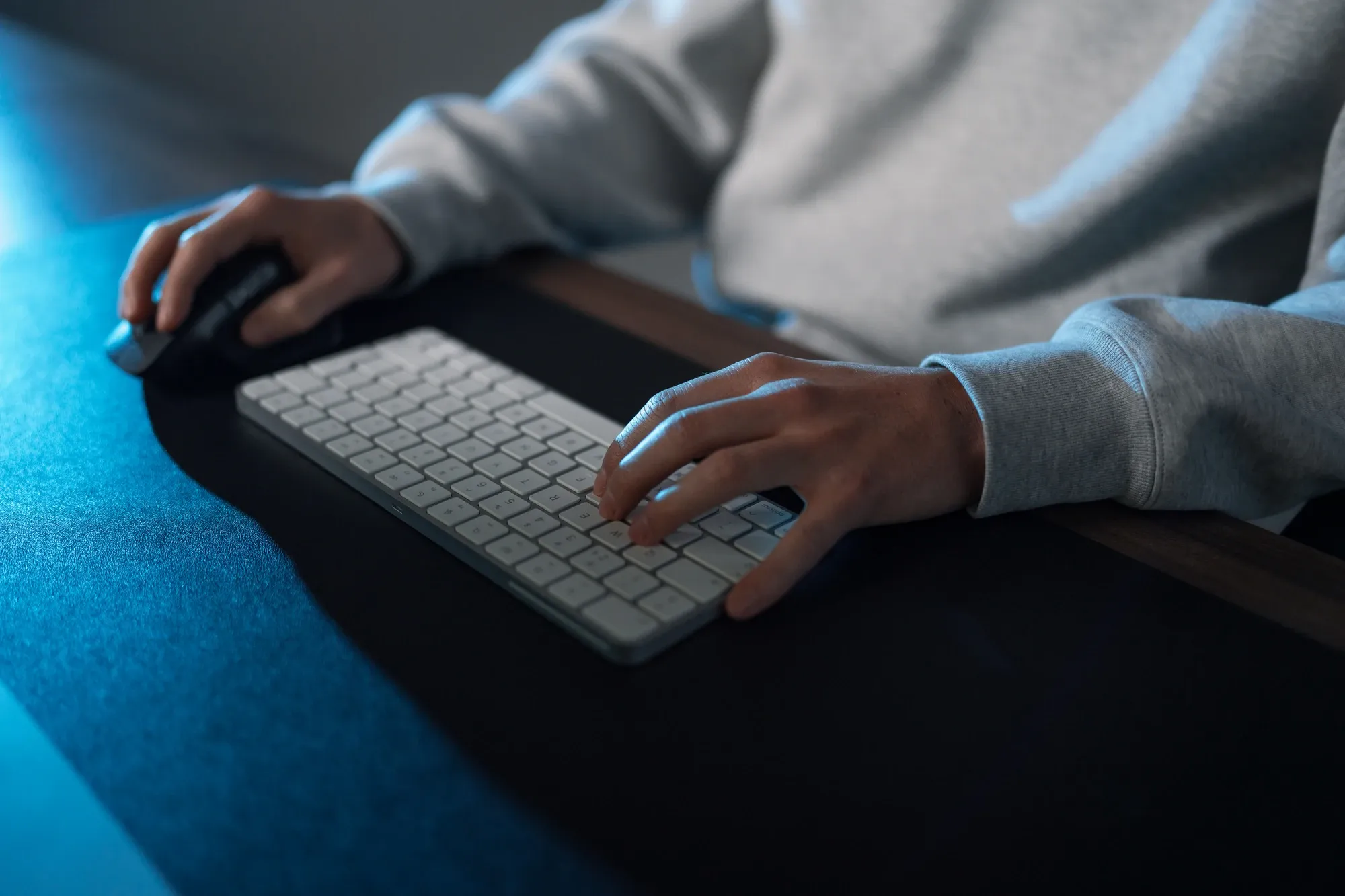 Handen op een wit toetsenbord en een muis, onder blauw licht op een bureau