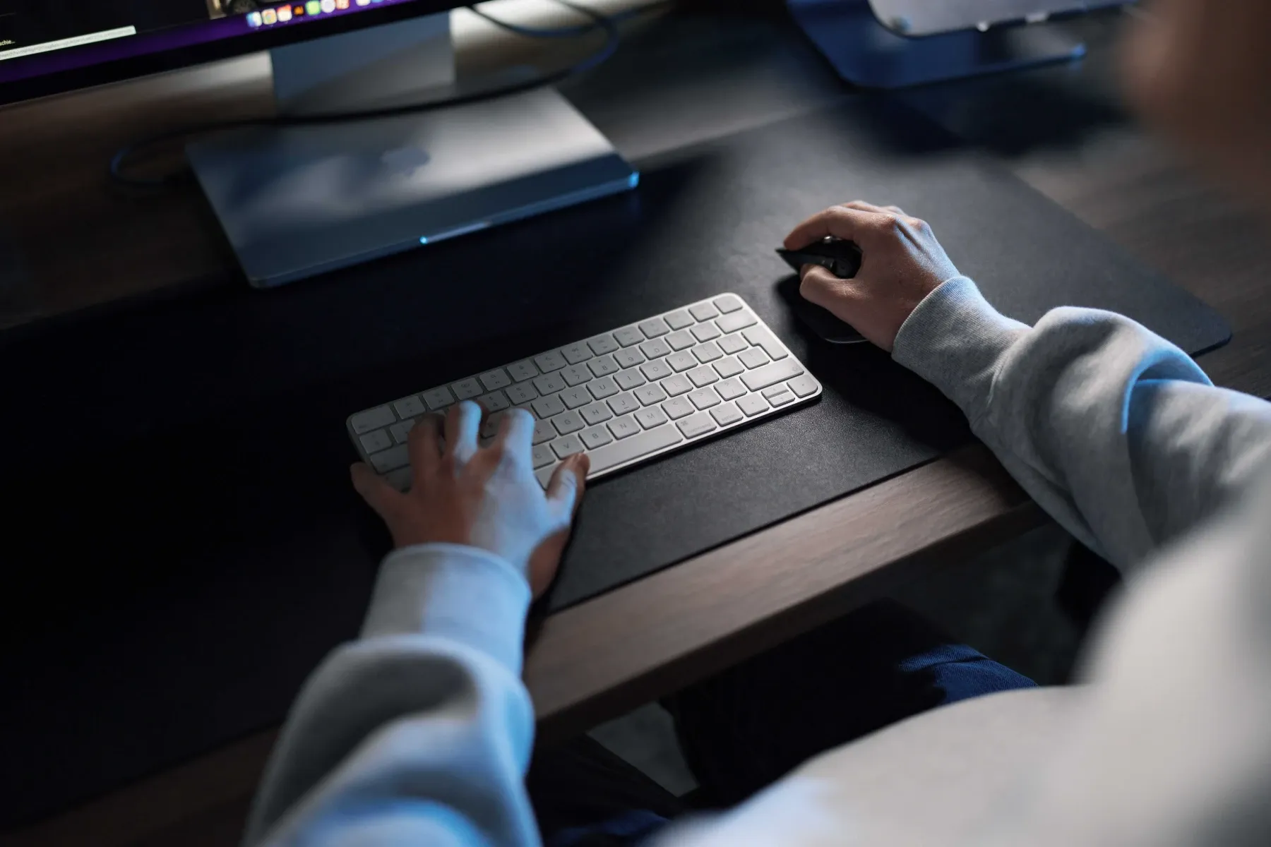 Handen op een toetsenbord en muis aan een bureau met een monitor, op kantoor bij Klubb
