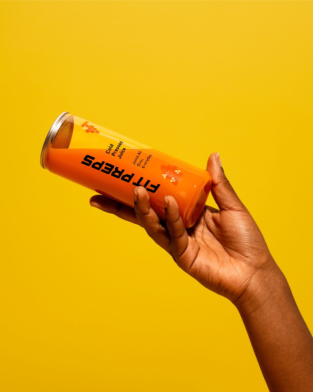 Hand houdt een fles cold pressed juice van Fit Preps omhoog tegen een gele achtergrond