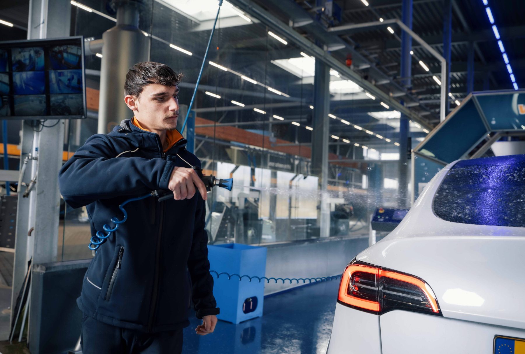 Medewerker van Washin7 spuit een auto af in de wasstraat