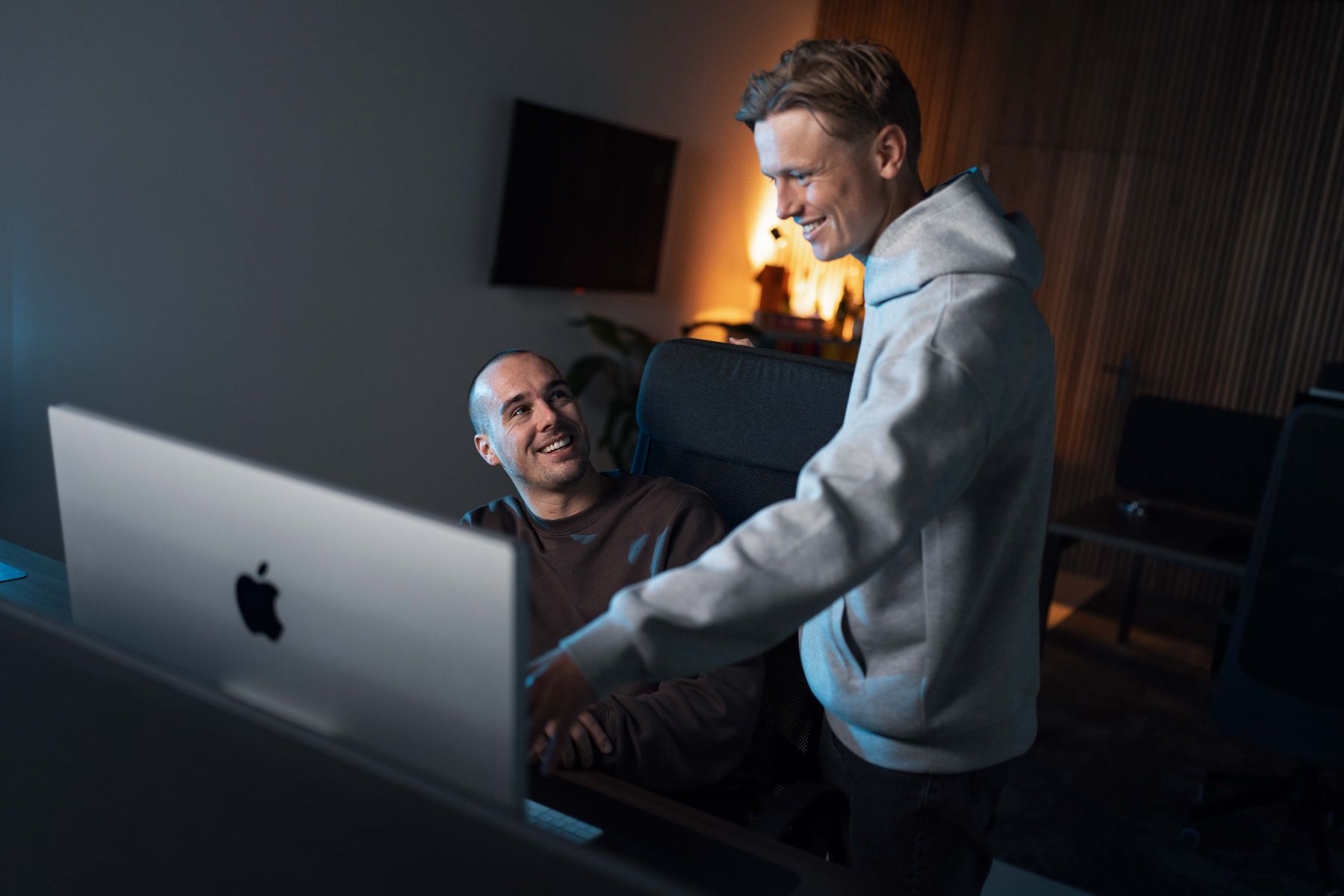 Twee specialisten van Klubb overleggen lachend achter een iMac op kantoor