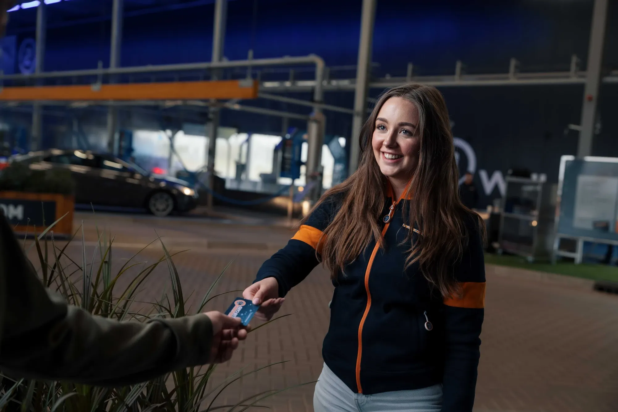 Medewerker van Washin7 overhandigt een klant een waspas bij de wasstraat