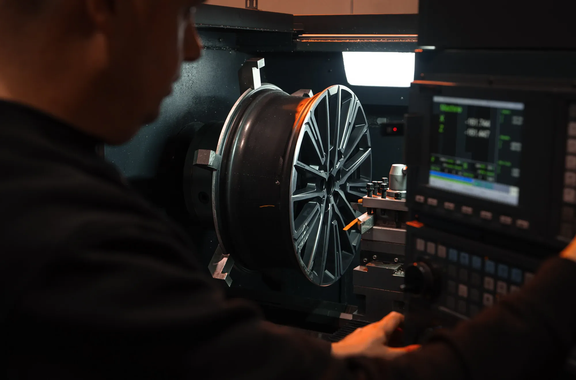 Medewerker van Wheelness bedient het scherm van de CNC-draaibank, met een velg in de klauwen