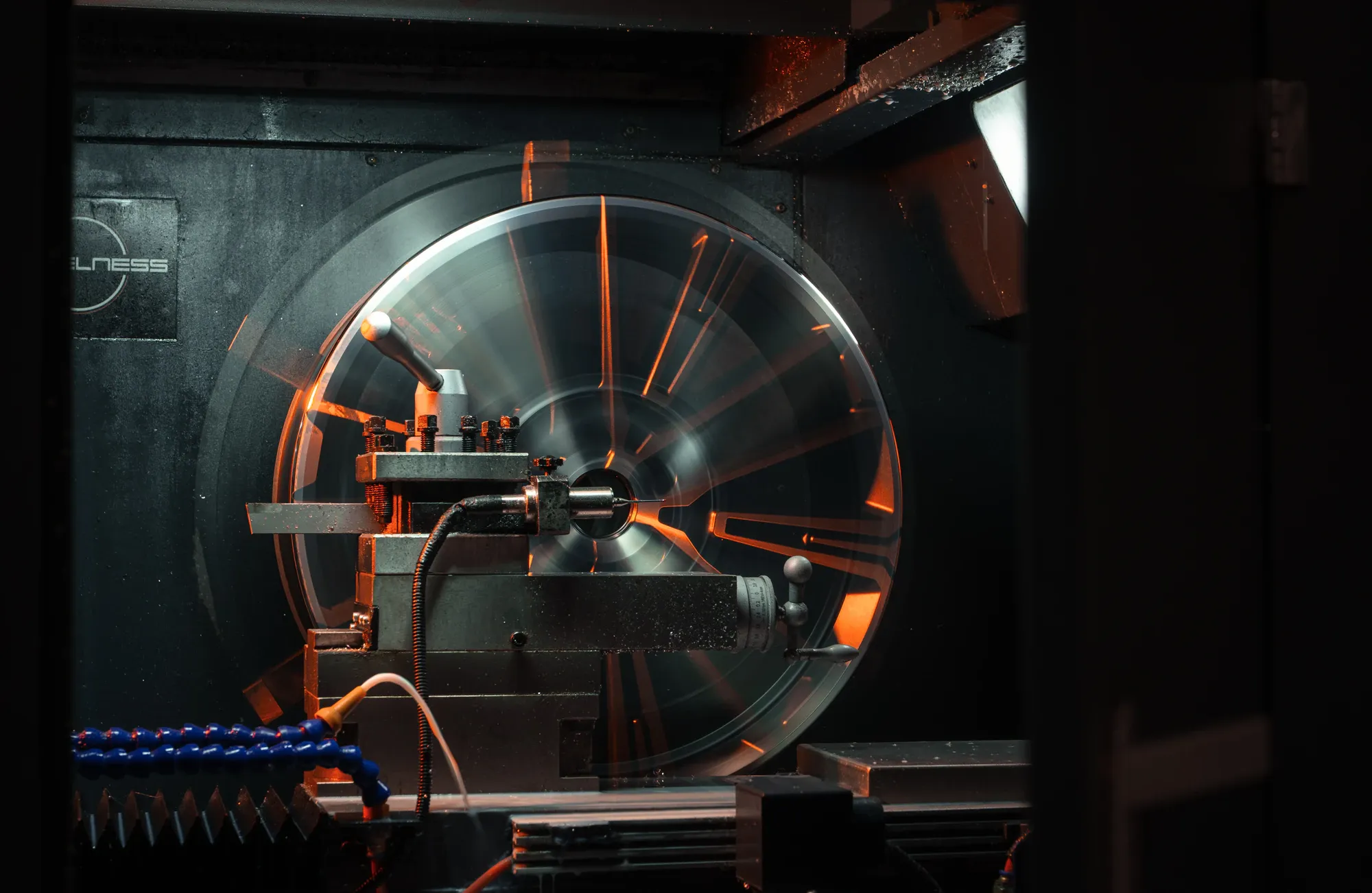Een velg draait in de CNC-draaibank van Wheelness, met oranje licht op de spaken en het logo op de wand erachter