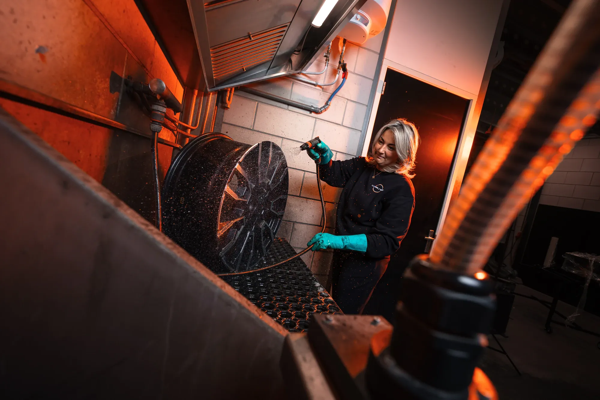 Medewerker van Wheelness in groene handschoenen spoelt een zwarte velg af met een tuinslang